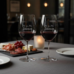Two wine glasses with 'Mr. & Mrs. Johanson' engraving on a table with appetizers and a candle.