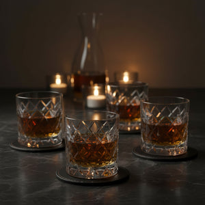 Four glasses of whiskey on a dark surface with candles in the background