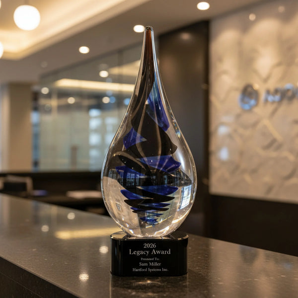 Glass award with blue interior on a black base, placed on a reflective surface with blurred office background.