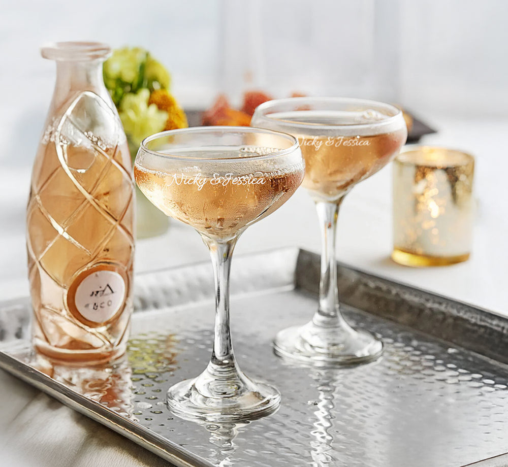 Two glasses of rose wine with a bottle on a tray, set against a blurred background.