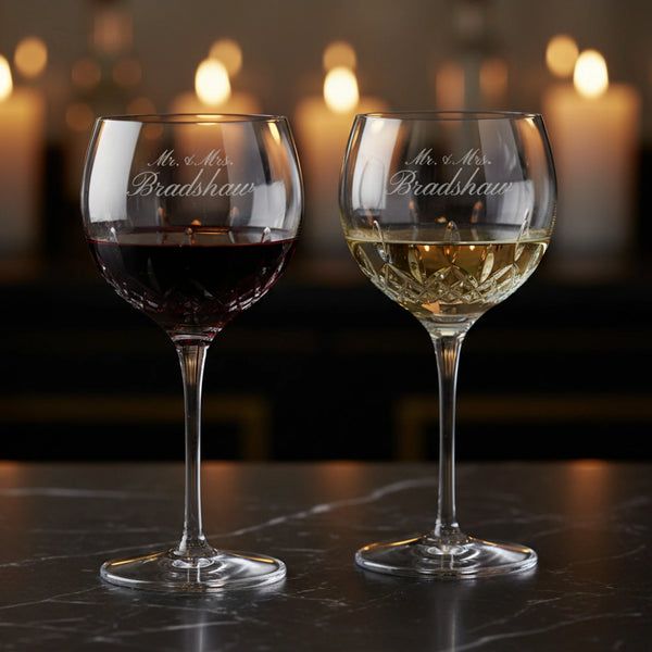 Two wine glasses with 'Mr. & Mrs. Bradshaw' engraving on a dark surface with blurred candles in the background.
